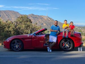 Father and two kids posing with a red Ferrari convertible in the Hollywood Hills during a family supercar experience in Los Angeles